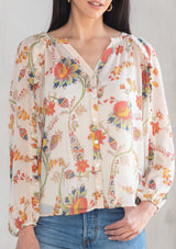 [Color: Ivory/Coral] A model wearing a sheer chiffon button front flowy bohemian top in a floral print. With long sleeves and ruffled trim. 