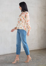 [Color: Ivory/Coral] A model wearing a sheer chiffon button front flowy bohemian top in a floral print. With long sleeves and ruffled trim. 