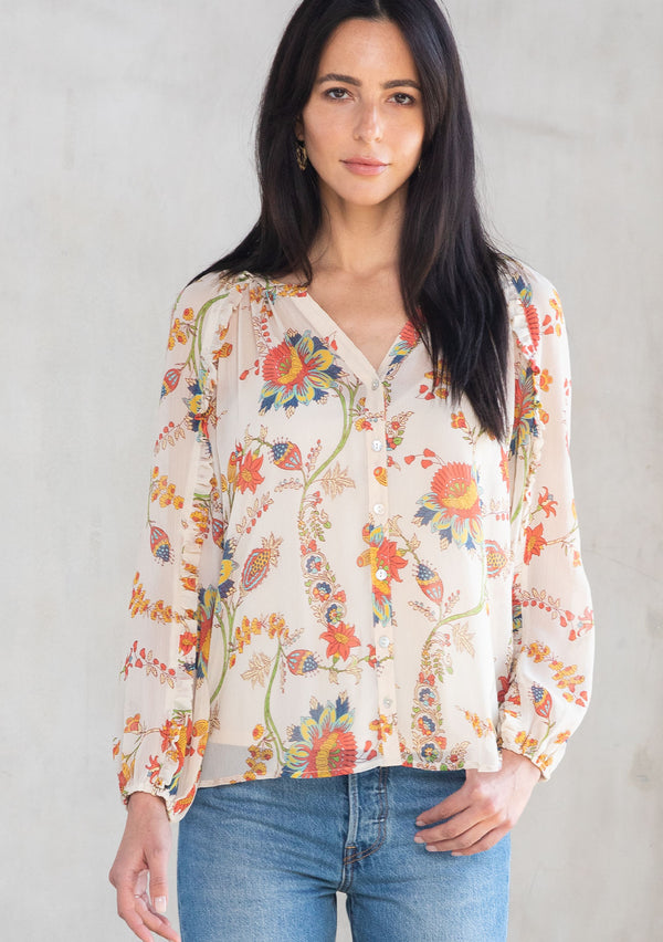 [Color: Ivory/Coral] A model wearing a sheer chiffon button front flowy bohemian top in a floral print. With long sleeves and ruffled trim. 