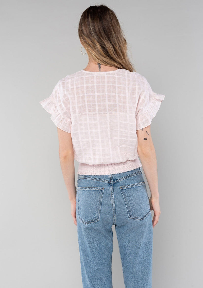 [Color: Light Pink] A back facing image of a blonde model wearing a light pink cotton bohemian top with short ruffled sleeves, a smocked elastic waist, and a surplice faux wrap front with a v neckline. 