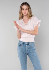 [Color: Light Pink] A front facing image of a blonde model wearing a light pink cotton bohemian top with short ruffled sleeves, a smocked elastic waist, and a surplice faux wrap front with a v neckline.