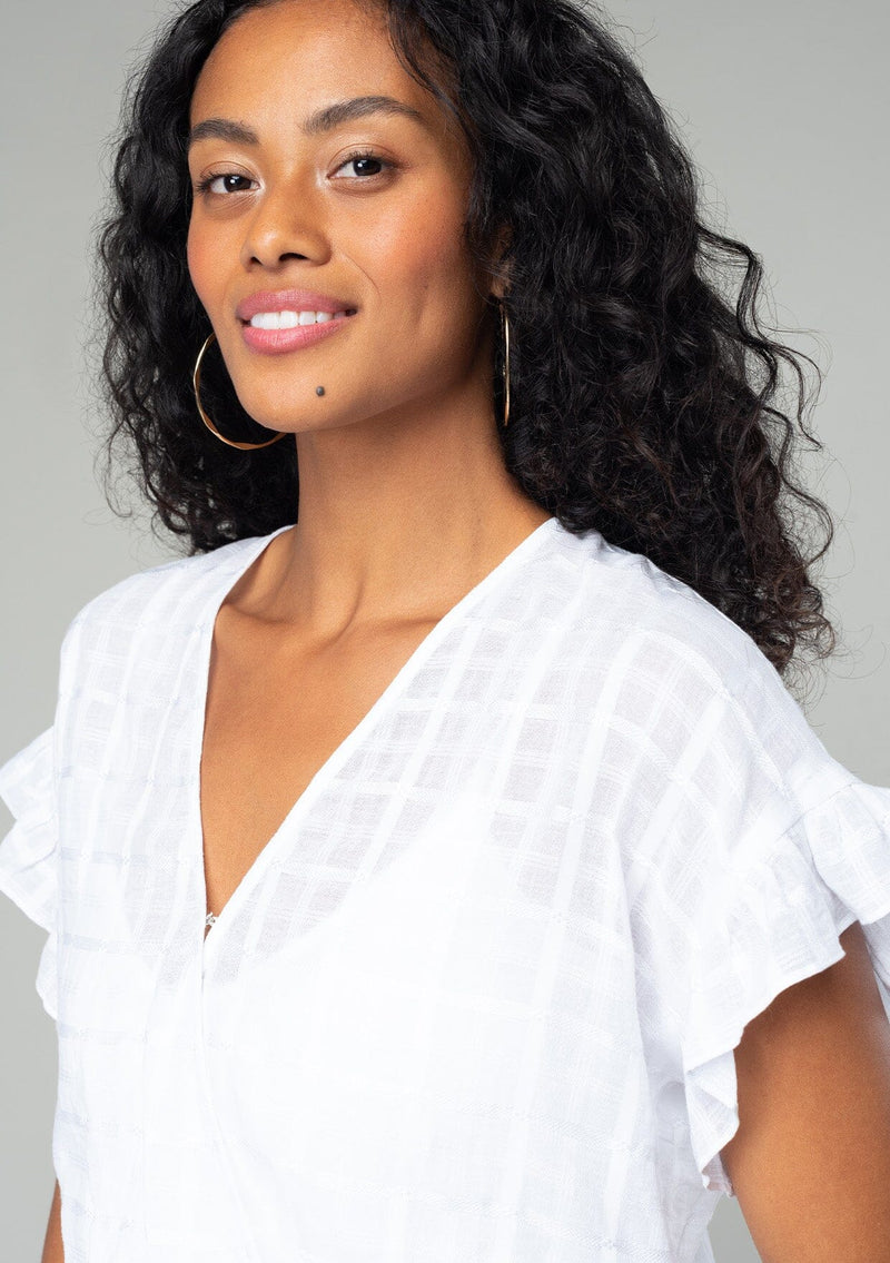 [Color: White] A close up front facing image of a brunette model wearing a bohemian white cotton top with short ruffled sleeves and a faux wrap front.