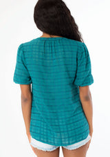 [Color: Teal] A back facing image of a black model wearing a bohemian teal cotton button front top with short puff sleeves.