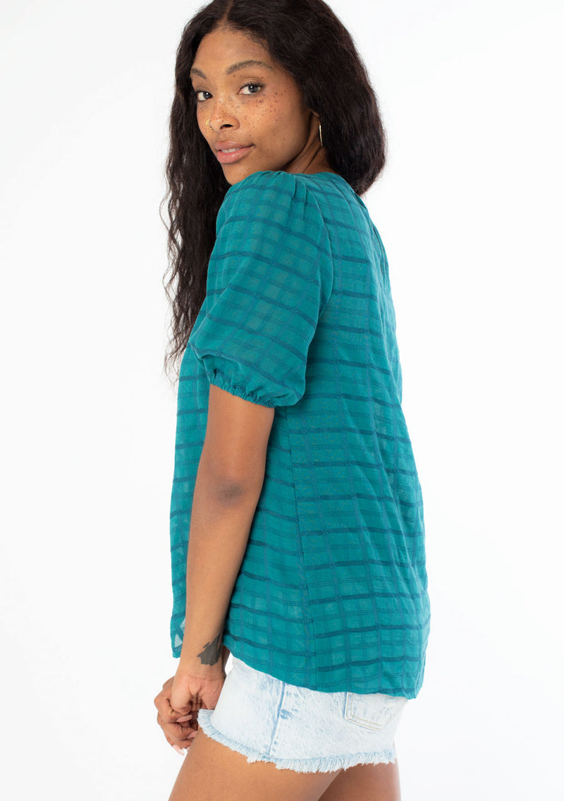 [Color: Teal] A side facing image of a black model wearing a bohemian teal cotton button front top with short puff sleeves.