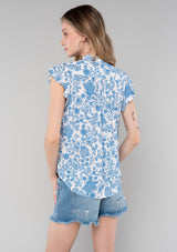 [Color: Cream/Dusty Blue] A back facing image of a blonde model wearing a classic best selling bohemian button front top in a cream and blue floral print. With short flutter cap sleeves and a ruffled neckline. 