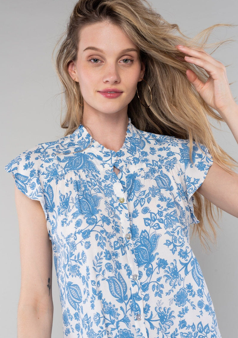 [Color: Cream/Dusty Blue] A close up front facing image of a blonde model wearing a classic best selling bohemian button front top in a cream and blue floral print. With short flutter cap sleeves and a ruffled neckline. 