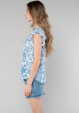 [Color: Cream/Dusty Blue] A side facing image of a blonde model wearing a classic best selling bohemian button front top in a cream and blue floral print. With short flutter cap sleeves and a ruffled neckline. 