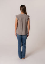 [Color: Cement] A back facing image of a brunette model wearing a grey crinkle gauze short sleeve flutter top with a button front and a ruffled neckline.
