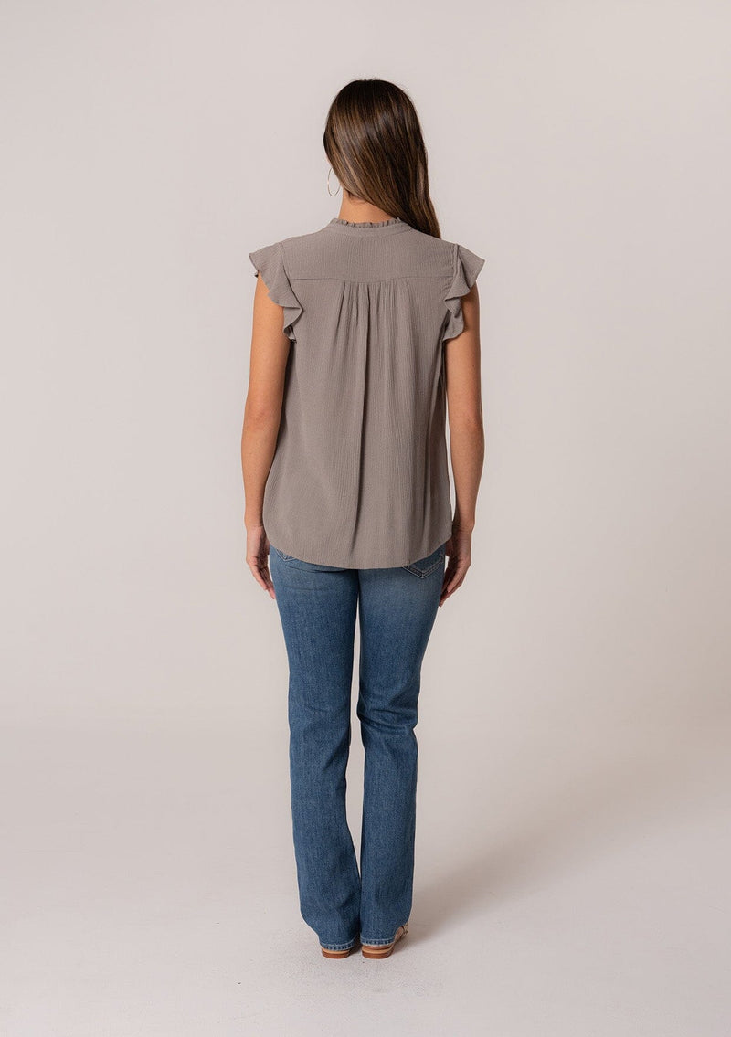 [Color: Cement] A back facing image of a brunette model wearing a grey crinkle gauze short sleeve flutter top with a button front and a ruffled neckline.