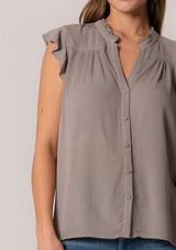 [Color: Cement] A close up front facing image of a brunette model wearing a grey crinkle gauze short sleeve flutter top with a button front and a ruffled neckline.