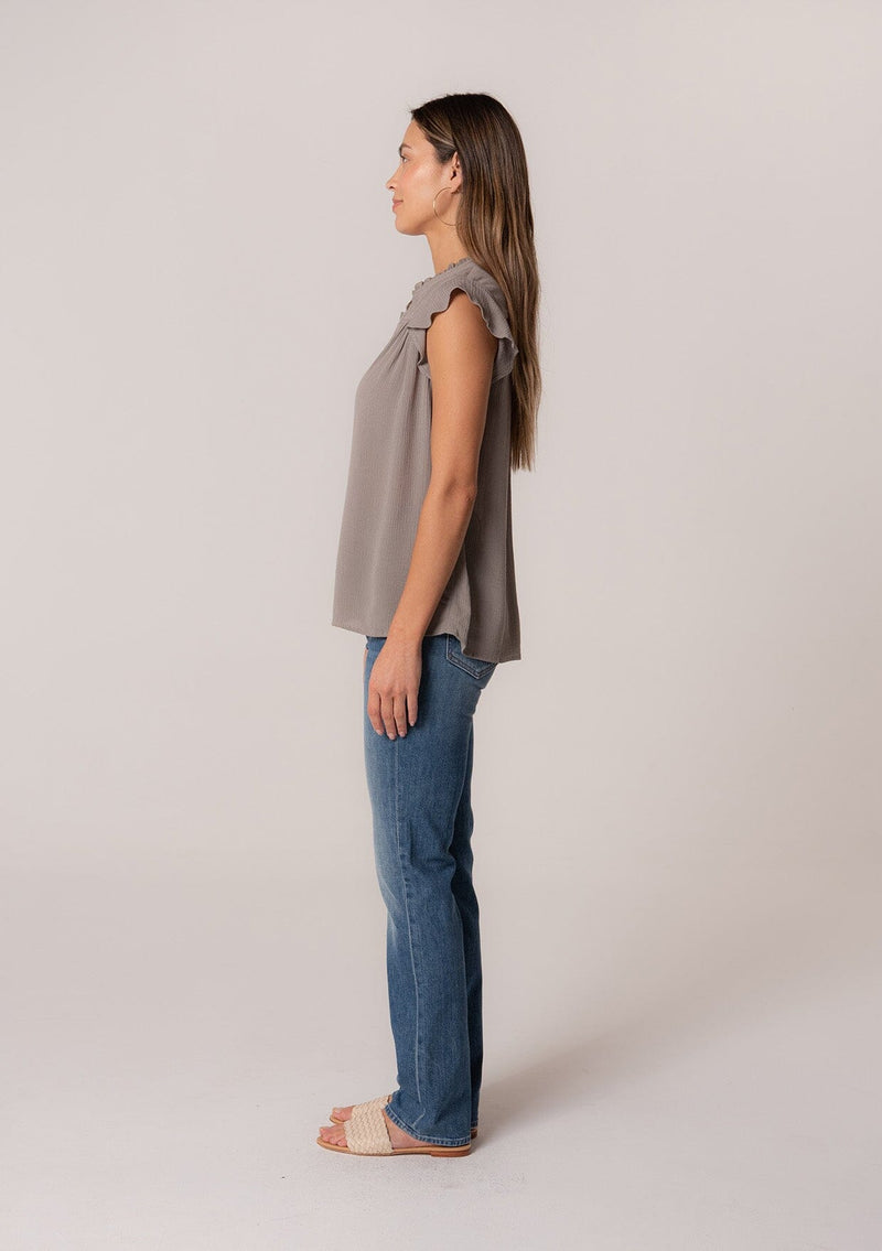 [Color: Cement] A side facing image of a brunette model wearing a grey crinkle gauze short sleeve flutter top with a button front and a ruffled neckline.