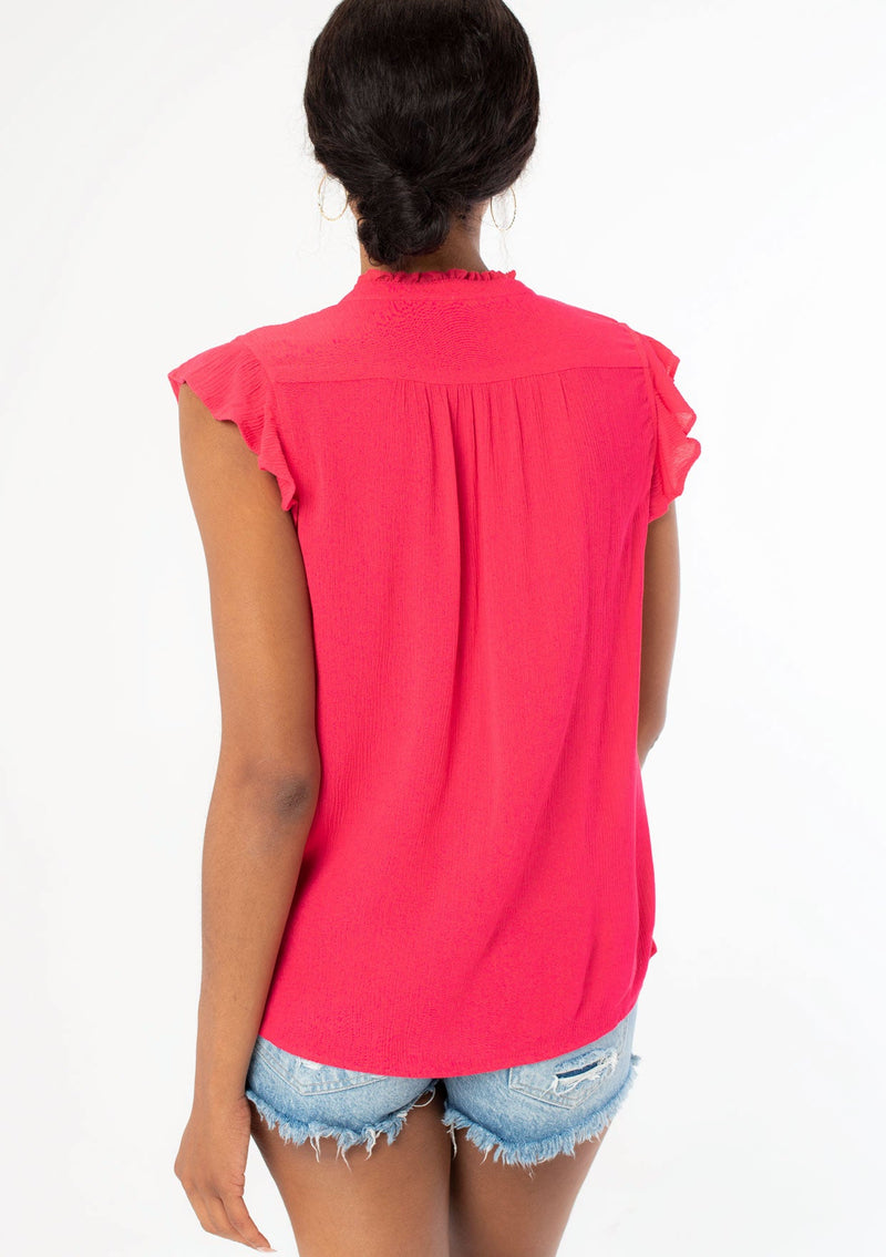 [Color: Hot Pink] A back facing image of a black model wearing a bright pink crinkle gauze short sleeve flutter top with a button front and a ruffled neckline.