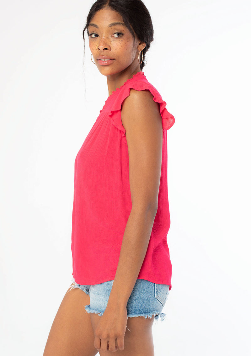 [Color: Hot Pink] A side facing image of a black model wearing a bright pink crinkle gauze short sleeve flutter top with a button front and a ruffled neckline.