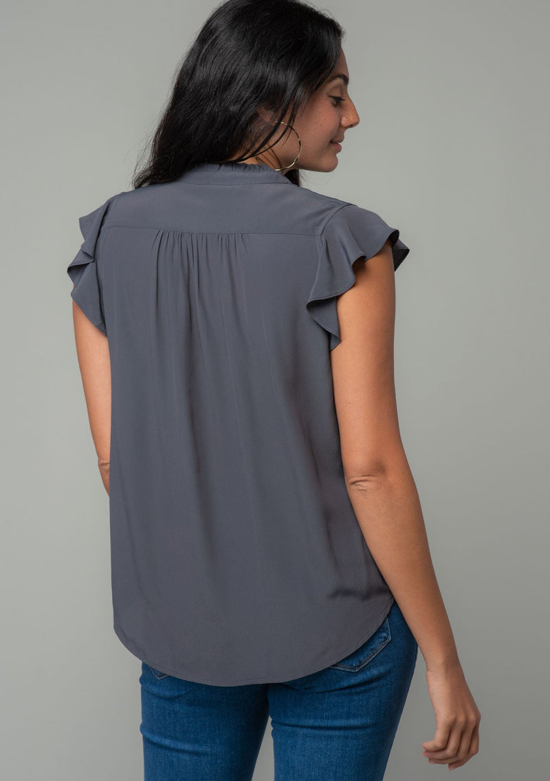 [Color: Pewter] A back facing image of a brunette model with long dark wavy hair wearing a classic bohemian short flutter sleeve button front top in a dark grey silky crepe. 