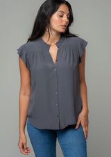 [Color: Pewter] A front facing image of a brunette model with long dark wavy hair wearing a classic bohemian short flutter sleeve button front top in a dark grey silky crepe. 