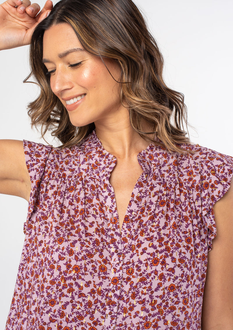 [Color: Lavender/Purple] A woman wearing a purple floral print bohemian button up top with short flutter sleeves and gold lurex details throughout. 