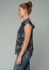 [Color: Charcoal/Dusty Blue] A side facing image of a red headed model wearing a bohemian navy blue top in a paisley dot print. With short ruffled sleeves, a button front, and a relaxed fit. 