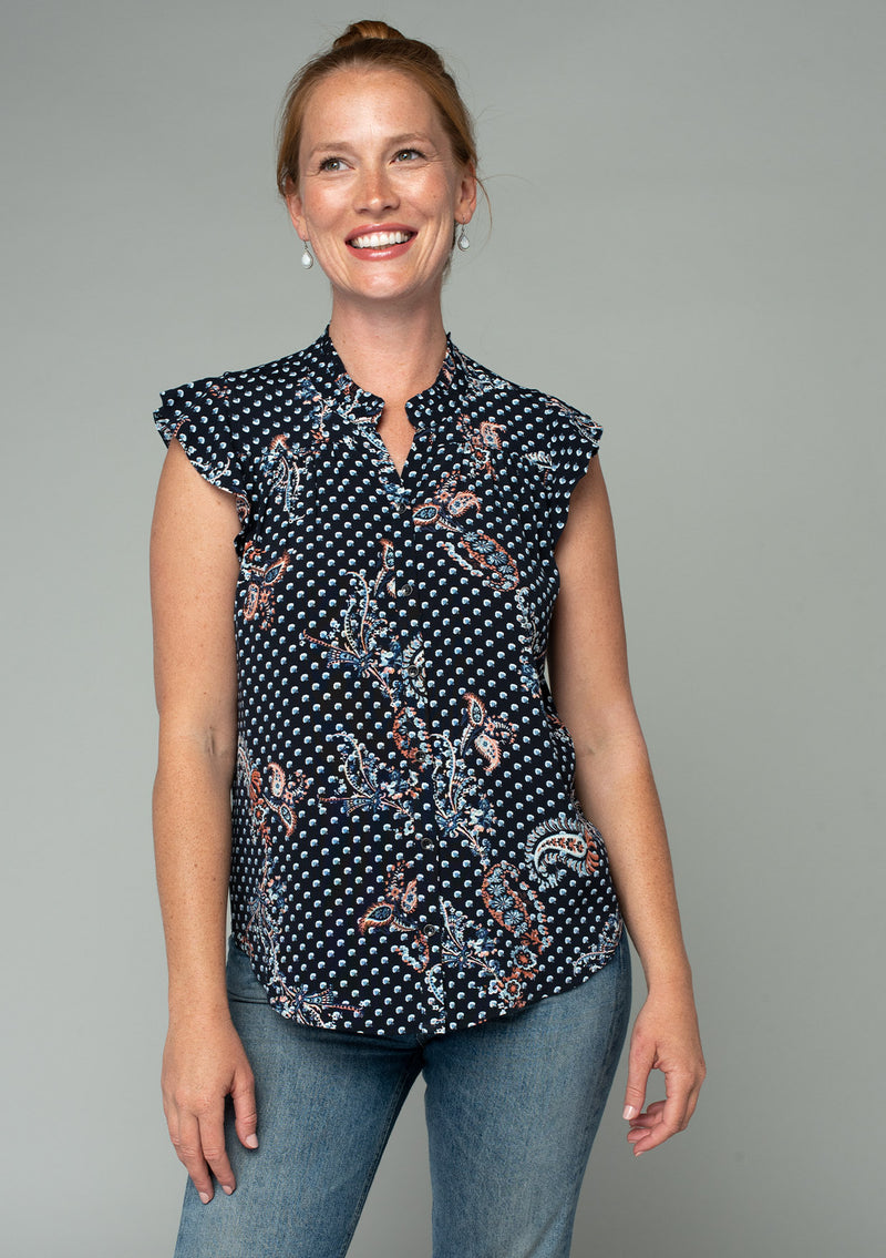 [Color: Charcoal/Dusty Blue] A half body front facing image of a red headed model wearing a bohemian navy blue top in a paisley dot print. With short ruffled sleeves, a button front, and a relaxed fit. 