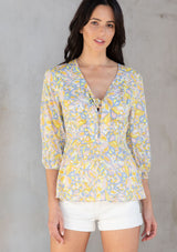 [Color: Blue/Lemon] A model wearing a blue and yellow retro floral print peplum top with a tie front detail. 