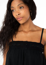 [Color: Black] A woman wearing a black flowy bohemian tank top with crochet trim, gold toned hardware, and adjustable spaghetti straps.