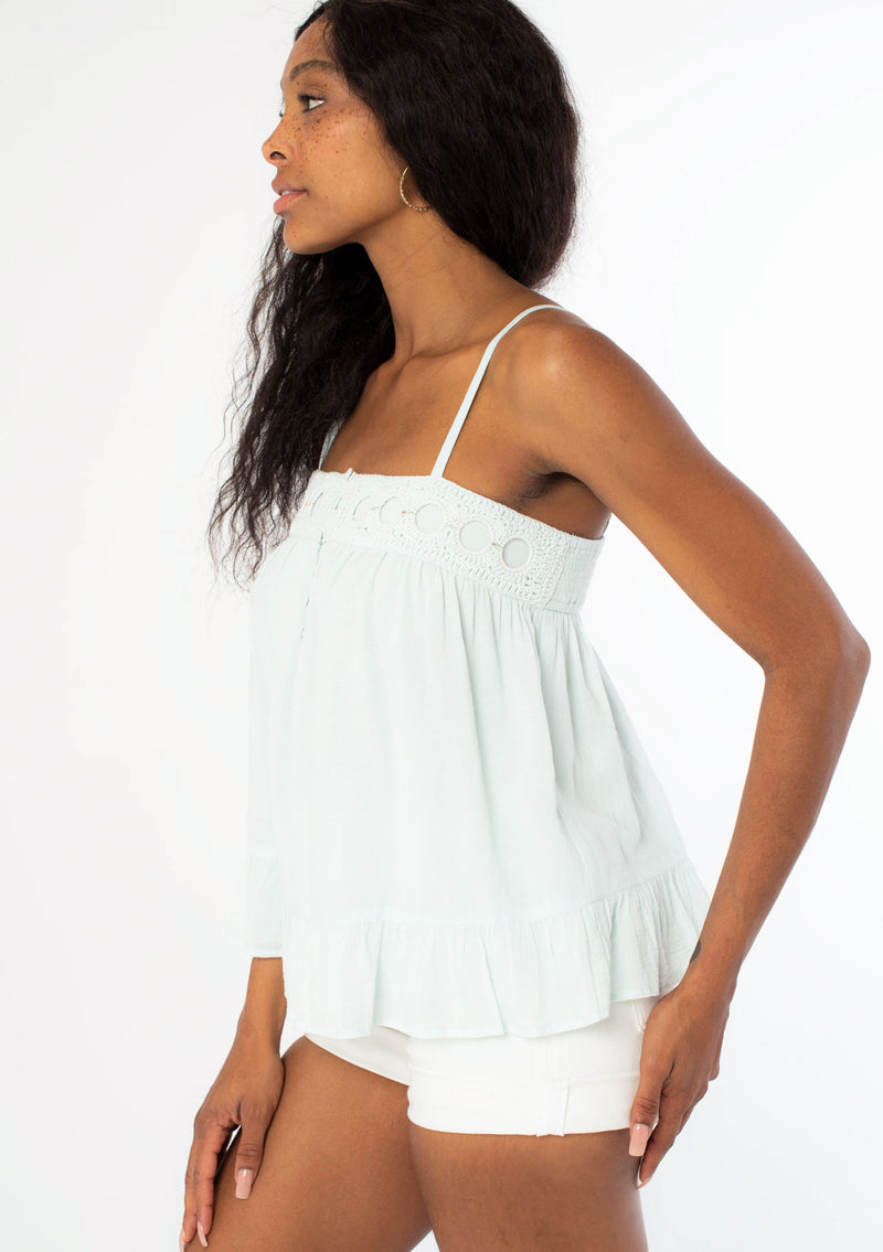 [Color: Aquamarine] A woman wearing a light teal flowy bohemian tank top with crochet trim, gold toned hardware, and adjustable spaghetti straps.