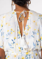 [Color: Cream/Yellow] A model wearing a white, yellow and blue floral print surplice top with short sleeves and a peplum waist. 