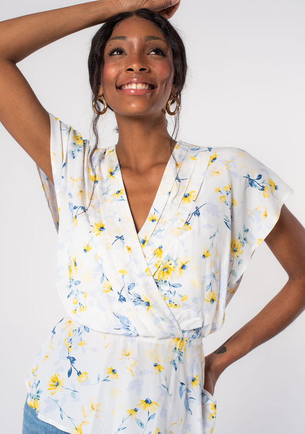 [Color: Cream/Yellow] A model wearing a white, yellow and blue floral print surplice top with short sleeves and a peplum waist. 