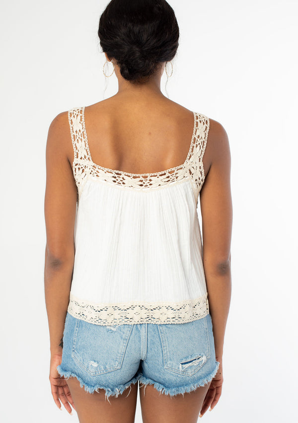 [Color: Off White/Natural] A back facing image of a black model wearing a white flowy cotton gauze tank top with natural crochet trim and crochet tank top straps. 
