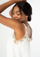 [Color: Off White/Natural] A close up side facing image of a black model wearing a white flowy cotton gauze tank top with natural crochet trim and crochet tank top straps. 