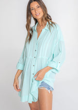 [Color: Mint] A model wearing a relaxed cotton tunic shirt with a button front, long rolled sleeves, and pleated details. 