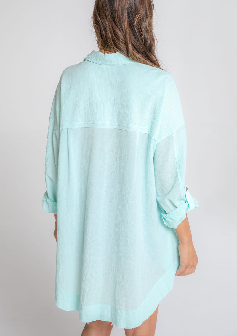 [Color: Mint] A model wearing a relaxed cotton tunic shirt with a button front, long rolled sleeves, and pleated details. 