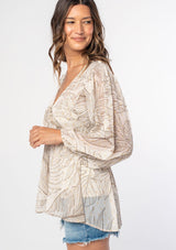 [Color: Natural/Taupe] A model wearing an off white leaf print sheer chiffon bohemian blouse with gold metallic clip dot details throughout. With long voluminous sleeves and a ruffle trimmed waist.