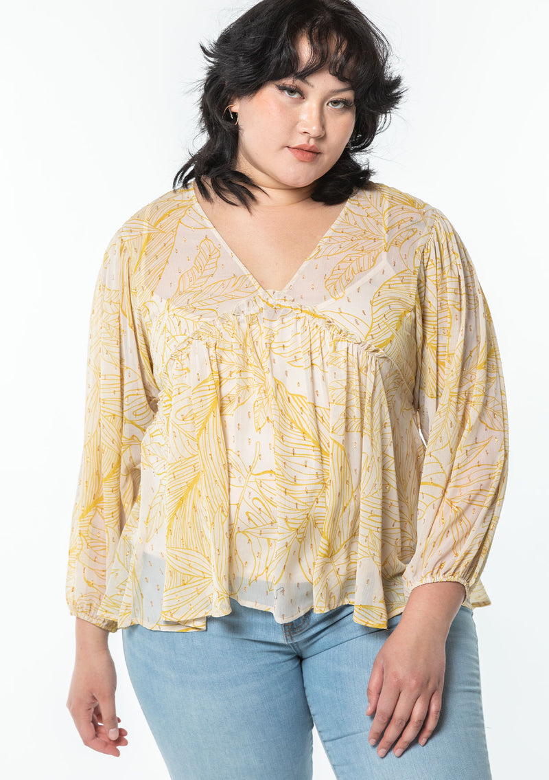 [Color: Natural/Mustard] A model wearing a yellow leaf print sheer chiffon bohemian blouse with gold metallic clip dot details throughout. With long voluminous sleeves and a ruffle trimmed waist.