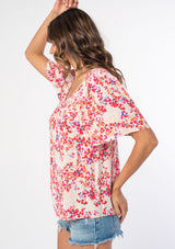 [Color: Blush/Red] A woman wearing a pink and red floral print bohemian top with short flutter sleeves, an open back, and a flowy, relaxed fit. 