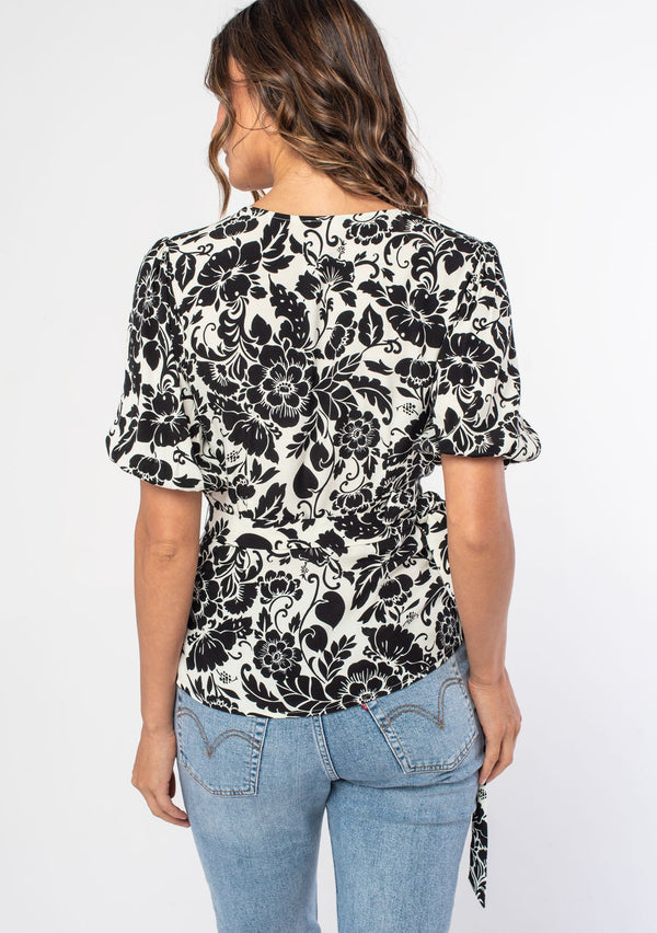 [Color: Ivory/Black] A woman wearing a white and black floral print bohemian wrap top with short puff sleeves. 