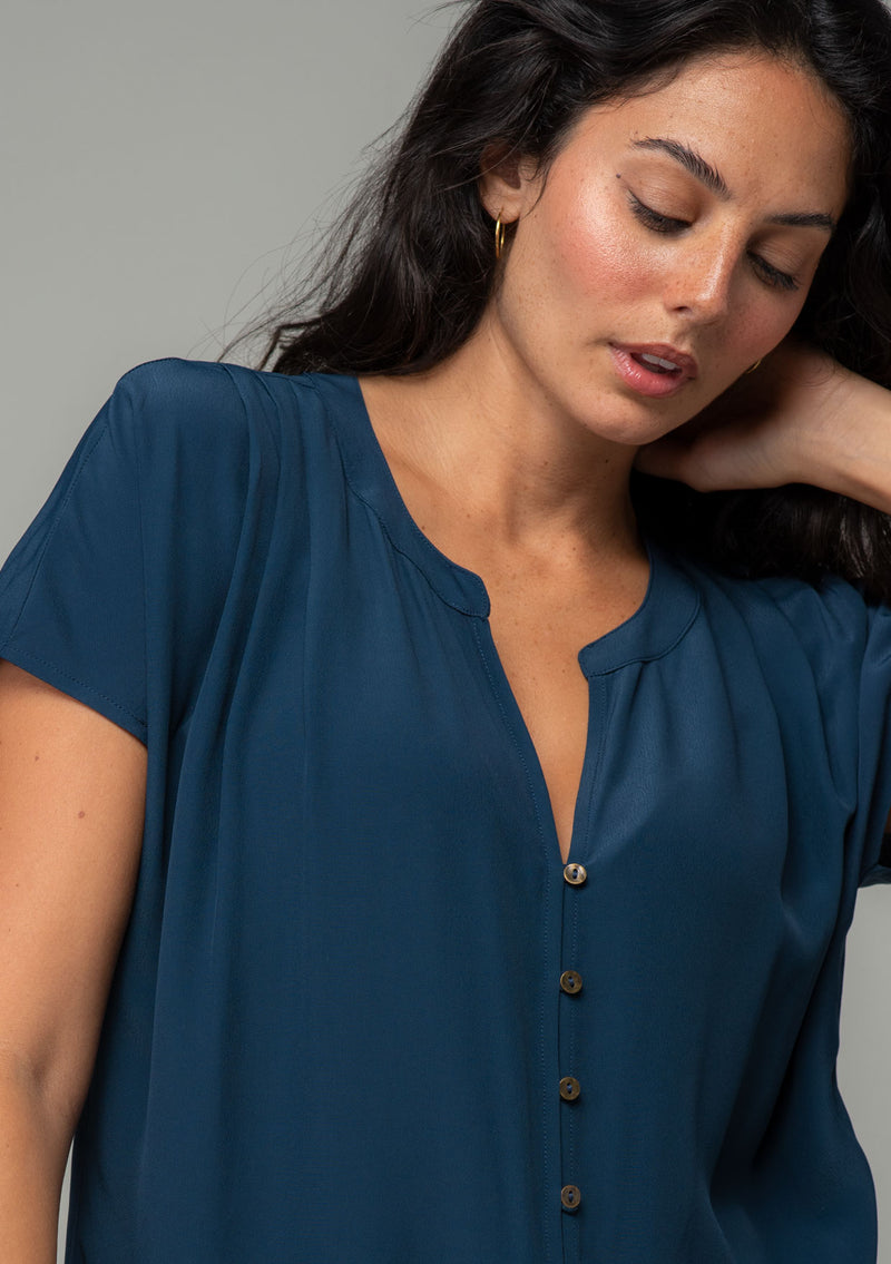 [Color: Midnight] A close up front facing image of a brunette model wearing a soft and silky navy blue short sleeve top with a button front and tie waist detail. 