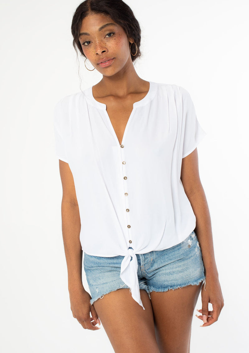 [Color: Chalk] A front facing image of a black model wearing a soft and silky white short sleeve top with a button front and tie waist detail. 
