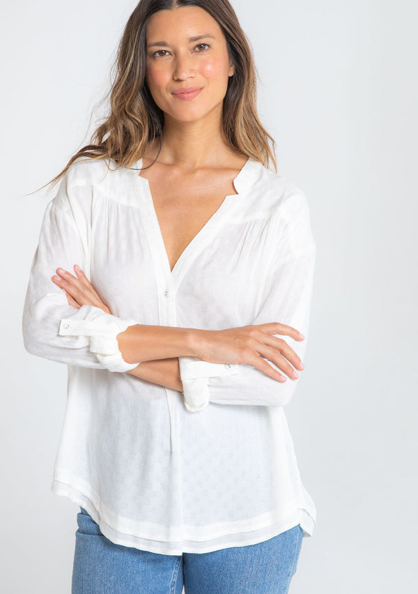 [Color: Chalk] A model wearing a classic lightweight white textured checkered jacquard long rolled tab sleeve blouse. With a notched v neckline and boxy relaxed fit.