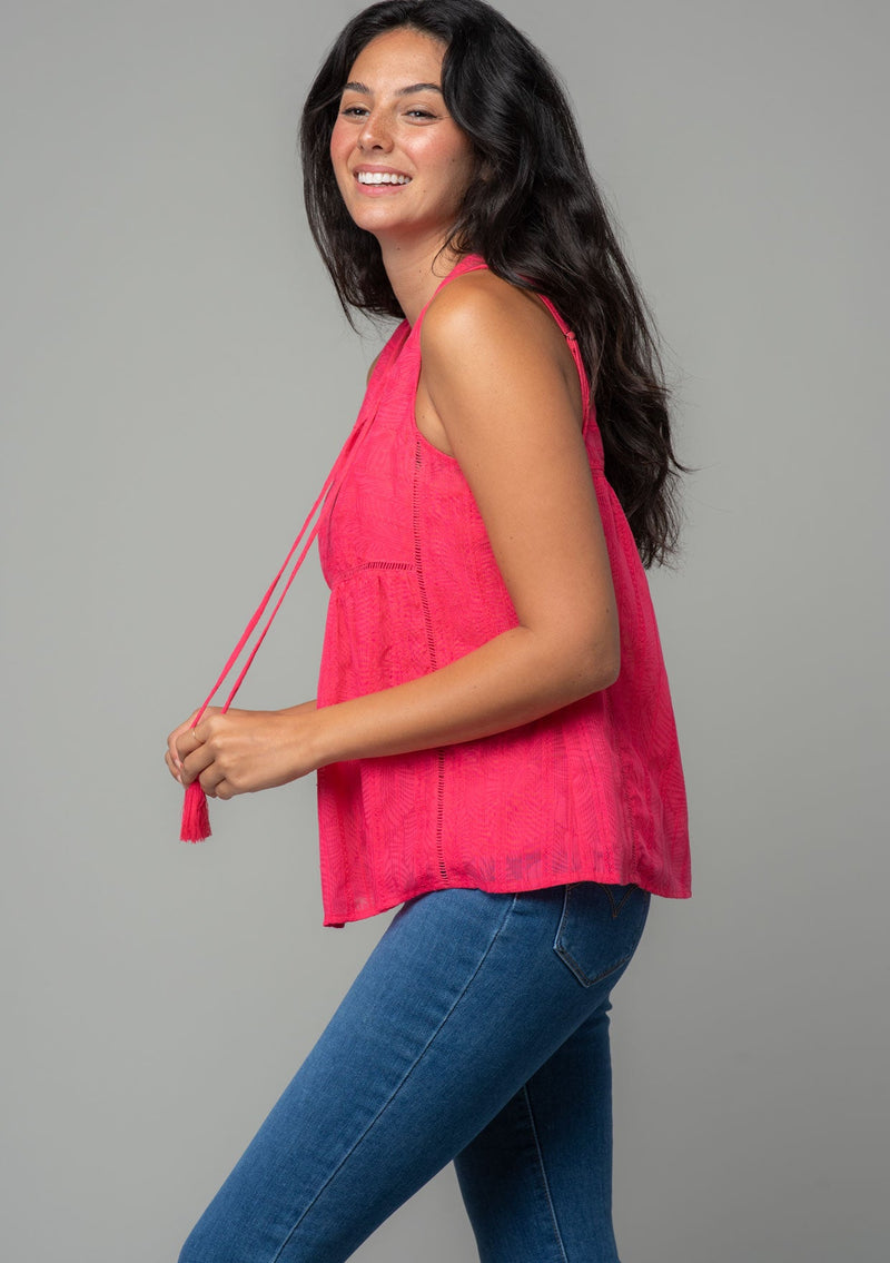 [Color: Watermelon] A side facing image of a brunette model with long wavy dark hair wearing a bright pink bohemian sleeveless tank top with a split v neckline and tassel ties.