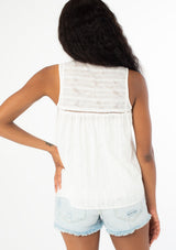 [Color: White] A back facing image of a black model with long wavy dark hair wearing a white bohemian sleeveless tank top with a split v neckline and tassel ties. 