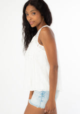[Color: White] A side facing image of a black model with long wavy dark hair wearing a white bohemian sleeveless tank top with a split v neckline and tassel ties. 