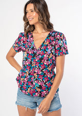 [Color: Black/Fuchsia] A woman wearing a black and pink floral print peplum top with short sleeves and a button front. 