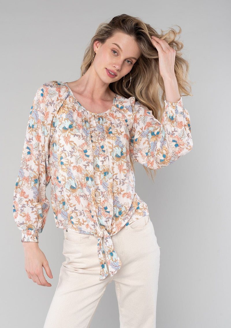 [Color: Natural/Coral] A front facing image of a blonde model wearing a bohemian blouse in a natural and coral floral print. With long sleeves, a round neckline, a self covered button front, and a tie front waist. 