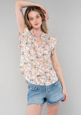 [Color: Natural/Coral] A front facing image of a blonde model wearing a classic bohemian popover top in a natural and coral floral print. With short flutter cap sleeves, a ruffled neckline with tassel ties, and a relaxed silhouette.