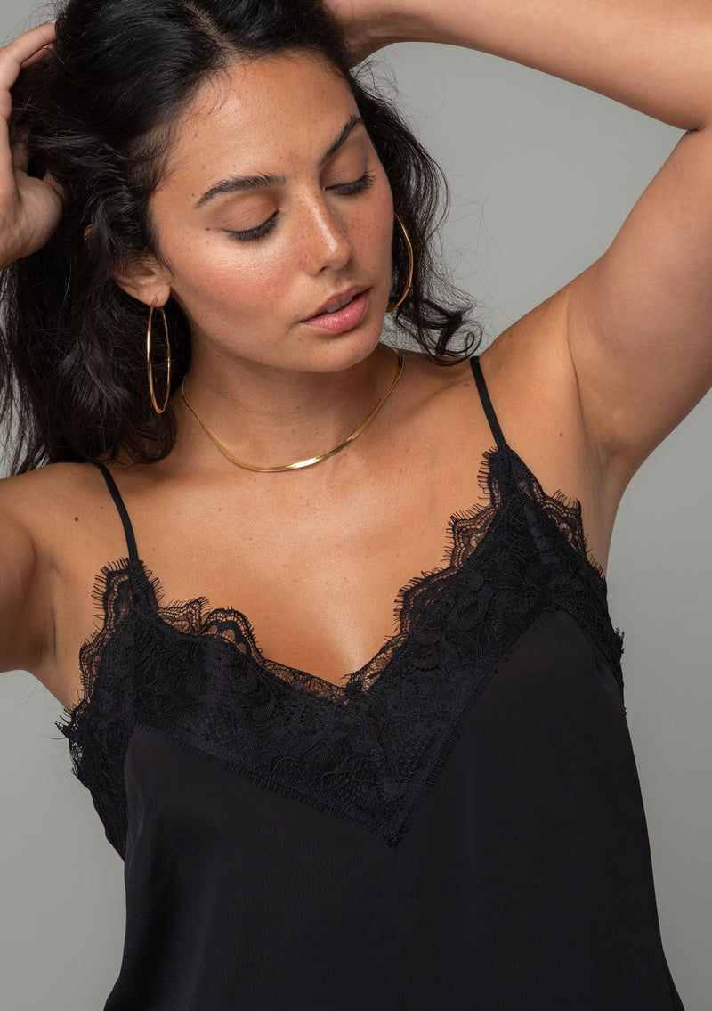 [Color: Black] A close up front facing image of a brunette model wearing a black lace trim camisole with a v neckline, adjustable spaghetti straps, and a flowy relaxed fit. 