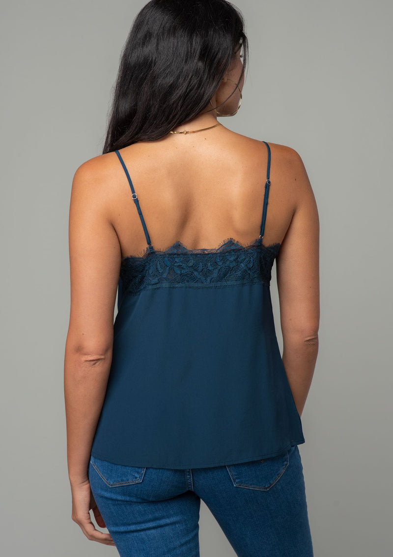 [Color: Midnight] A back facing image of a brunette model wearing a navy blue lace trim camisole with a v neckline, adjustable spaghetti straps, and a flowy relaxed fit. 