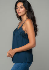 [Color: Midnight] A side facing image of a brunette model wearing a navy blue lace trim camisole with a v neckline, adjustable spaghetti straps, and a flowy relaxed fit. 