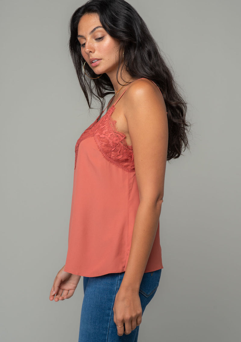 [Color: Rosewood] A side facing image of a brunette model wearing a dusty rose pink lace trim camisole with a v neckline, adjustable spaghetti straps, and a flowy relaxed fit. 