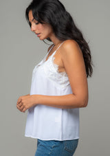 [Color: Chalk] A side facing image of a brunette model wearing a white lace trim camisole with a v neckline, adjustable spaghetti straps, and a flowy relaxed fit. 