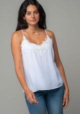 [Color: Chalk] A front facing image of a brunette model wearing a white lace trim camisole with a v neckline, adjustable spaghetti straps, and a flowy relaxed fit. 